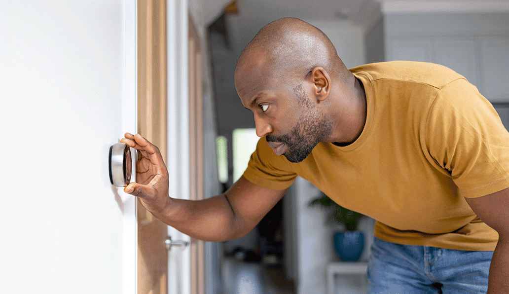 Young African American man wearing a yellow t-shirt adjusting smart thermostat temperature