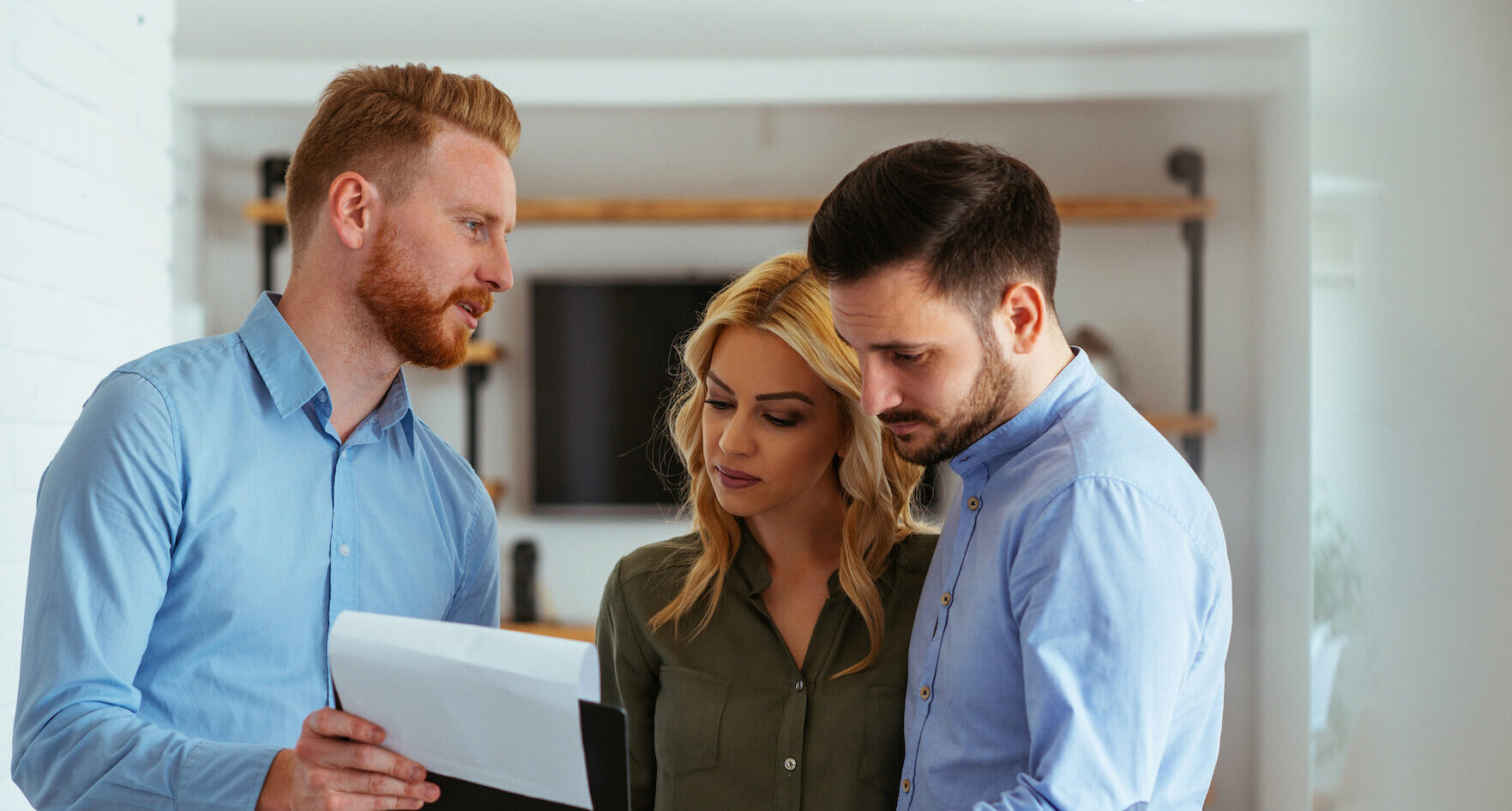 Close up photo of a woman and two men inside of an office holding and looking at a black writing pad
