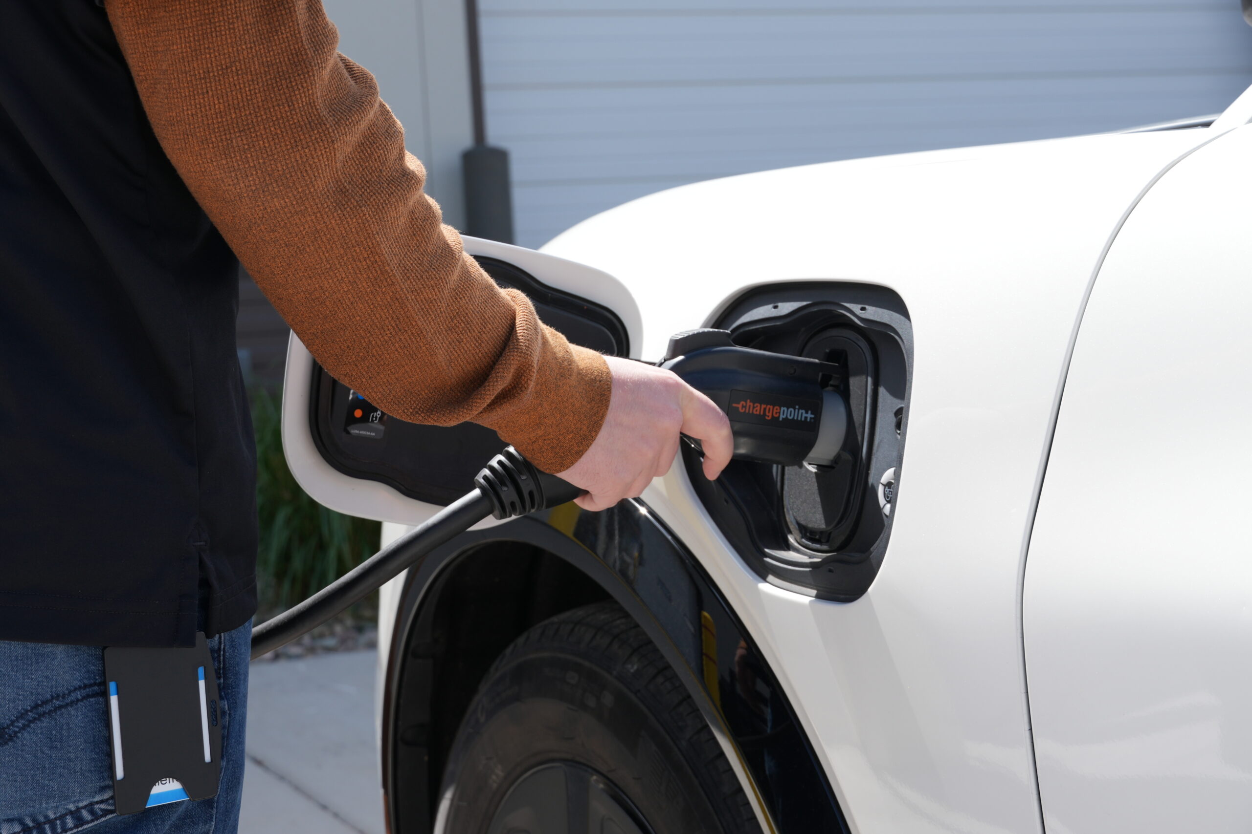 Close up of a man plugging in an electric charger to a white electric vehicle