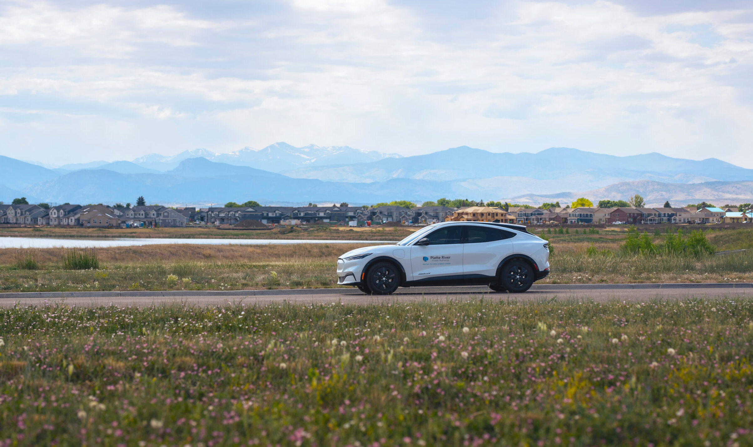 White electric vehicle driving on a road with a field of wildflowers.