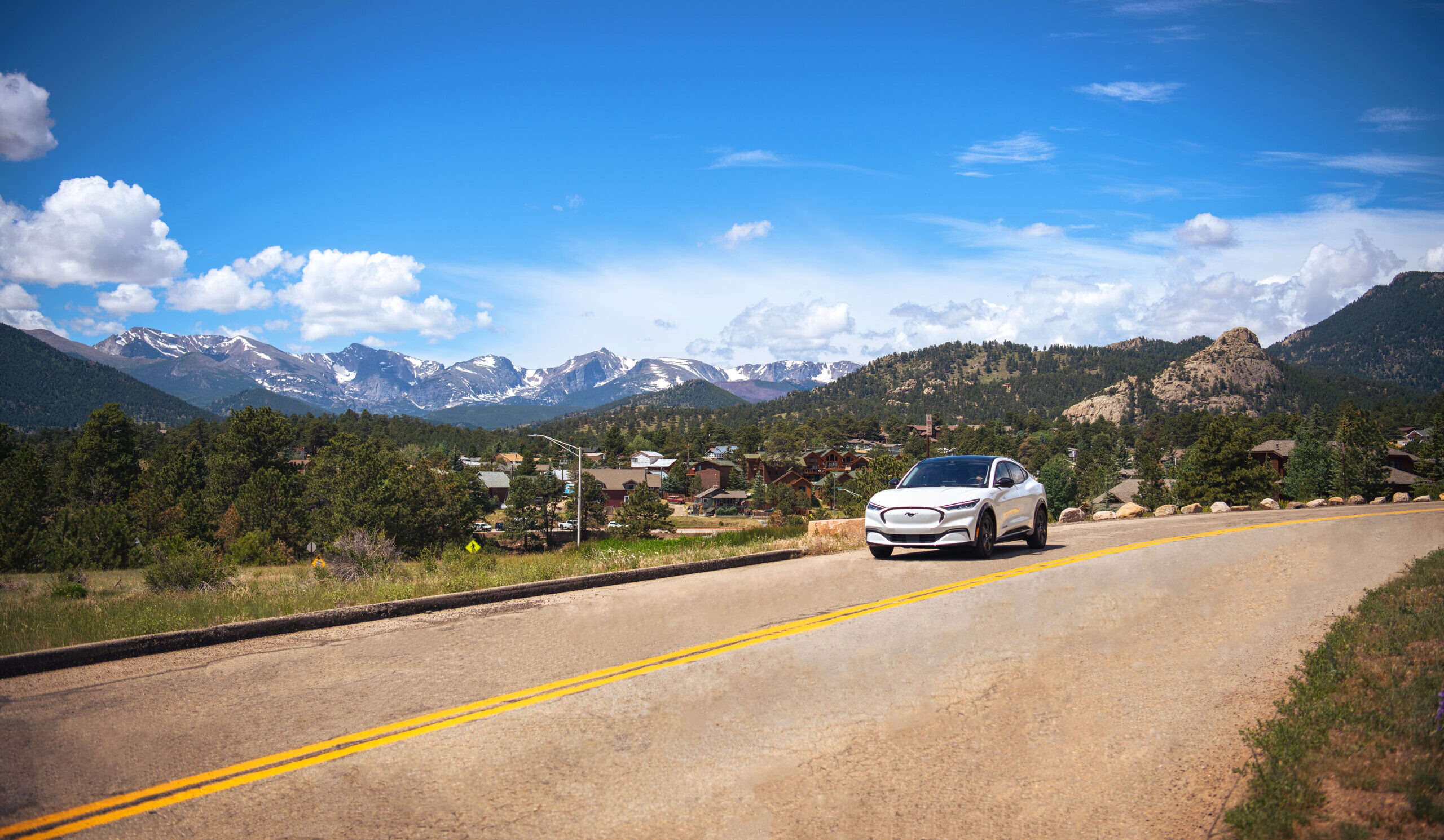 Wide shot of a white electric vehicle driving through Estes Park