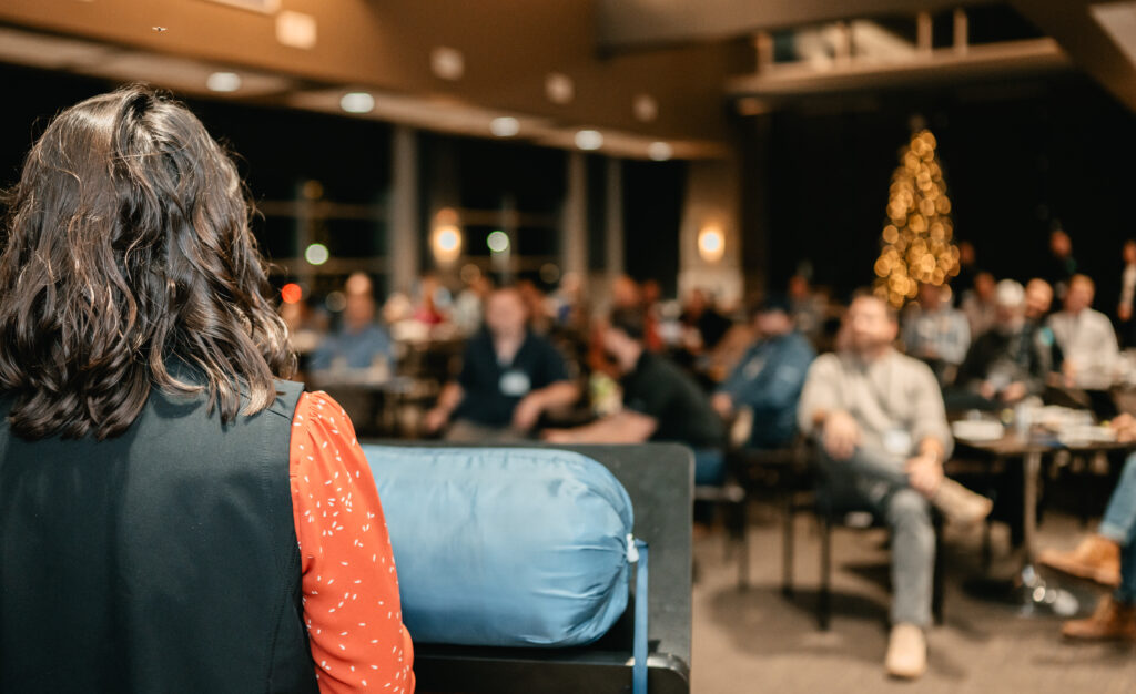 Photo of the back of a young woman presenting to a crowd at an event.