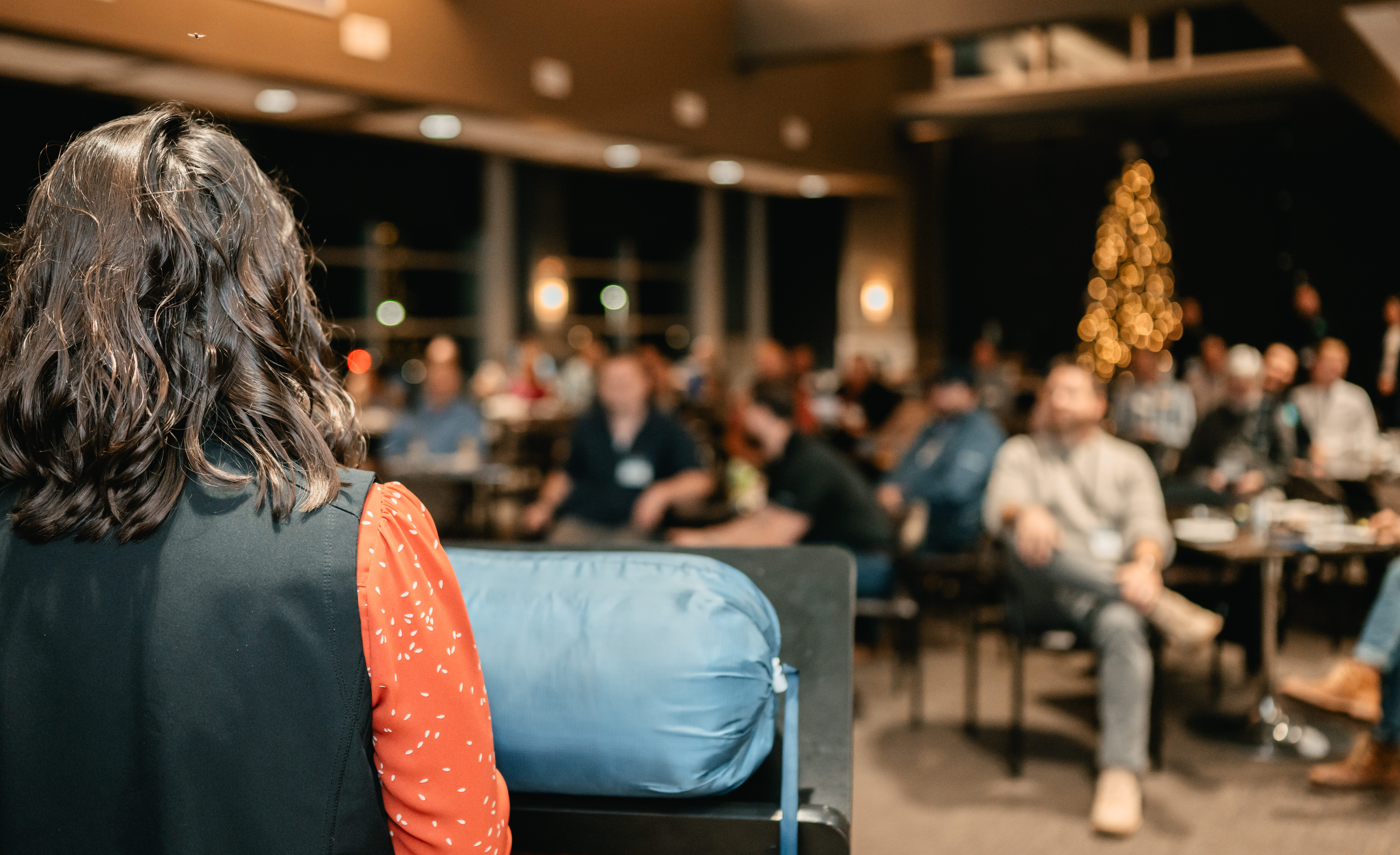 Photo of the back of a young woman presenting to a crowd at an event.