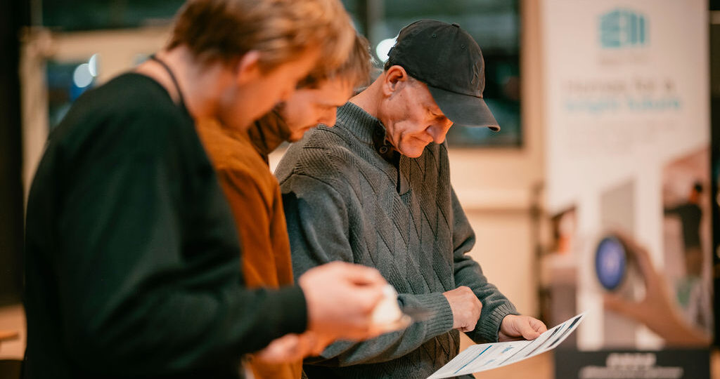 Three men looking at and holding an Efficiency Works flyer.