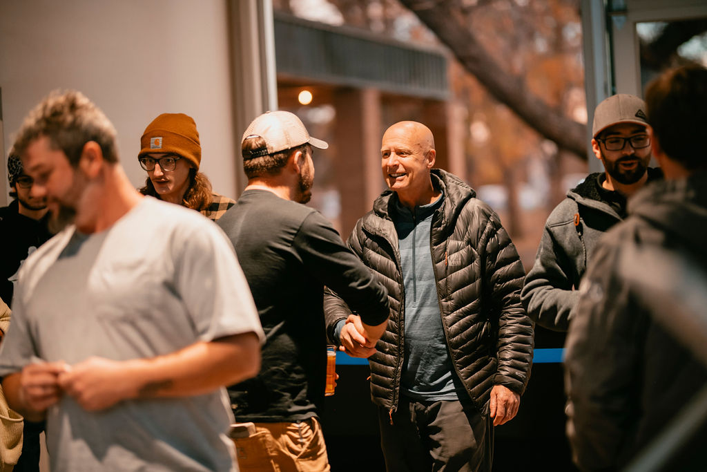 Two men shaking hands at an event amongst a crowd.
