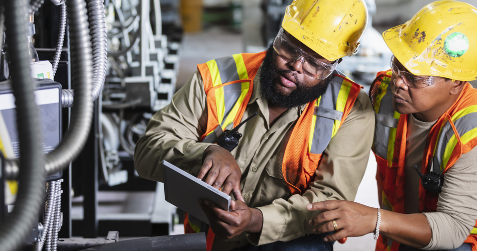 Two young men looking at a tablet while doing machinery work.
