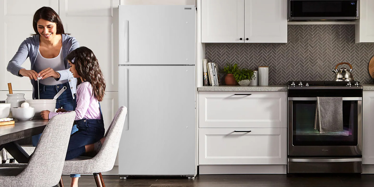 Wide shot of a white kitchen with a mother breaking an egg into a white bowl on a table in front of her daughter