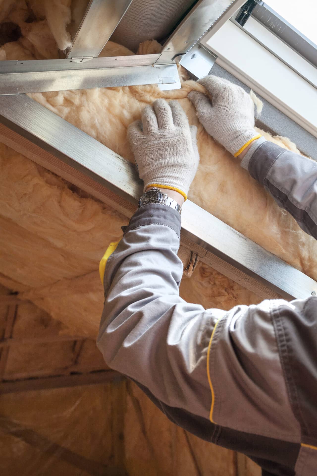 Hand of a professional worker in protective gloves putting mineral rockwool insulation in wall near windows, behind wooden plank boards.