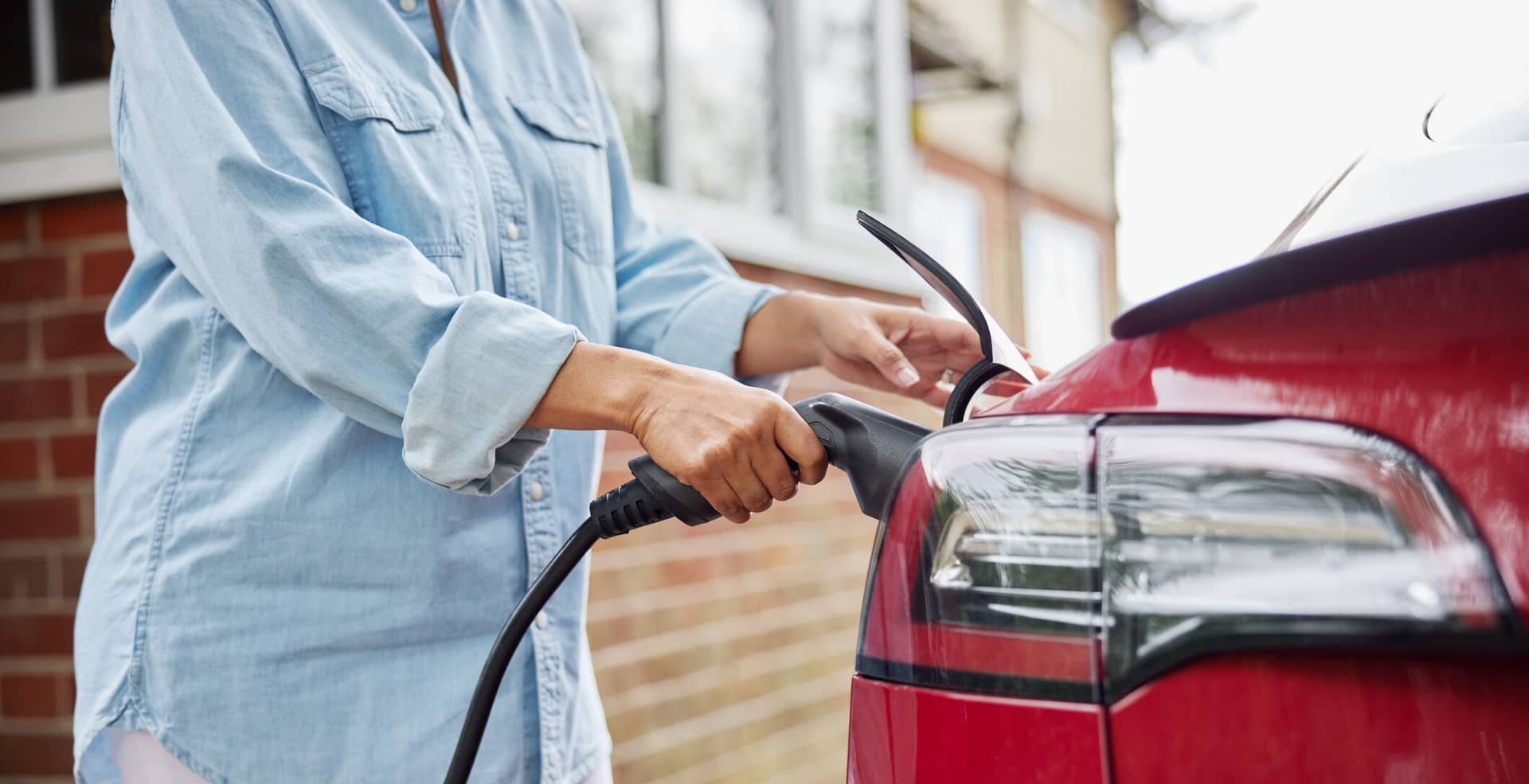 Close Up Of Woman Attaching Charging Cable To Environmentally Friendly Zero Emission Electric Car At Home