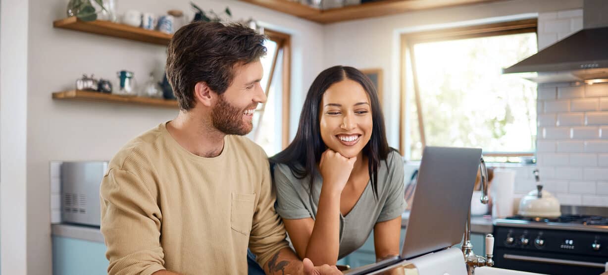 Happy young man working on laptop while his wife stands next to him looking at the screen