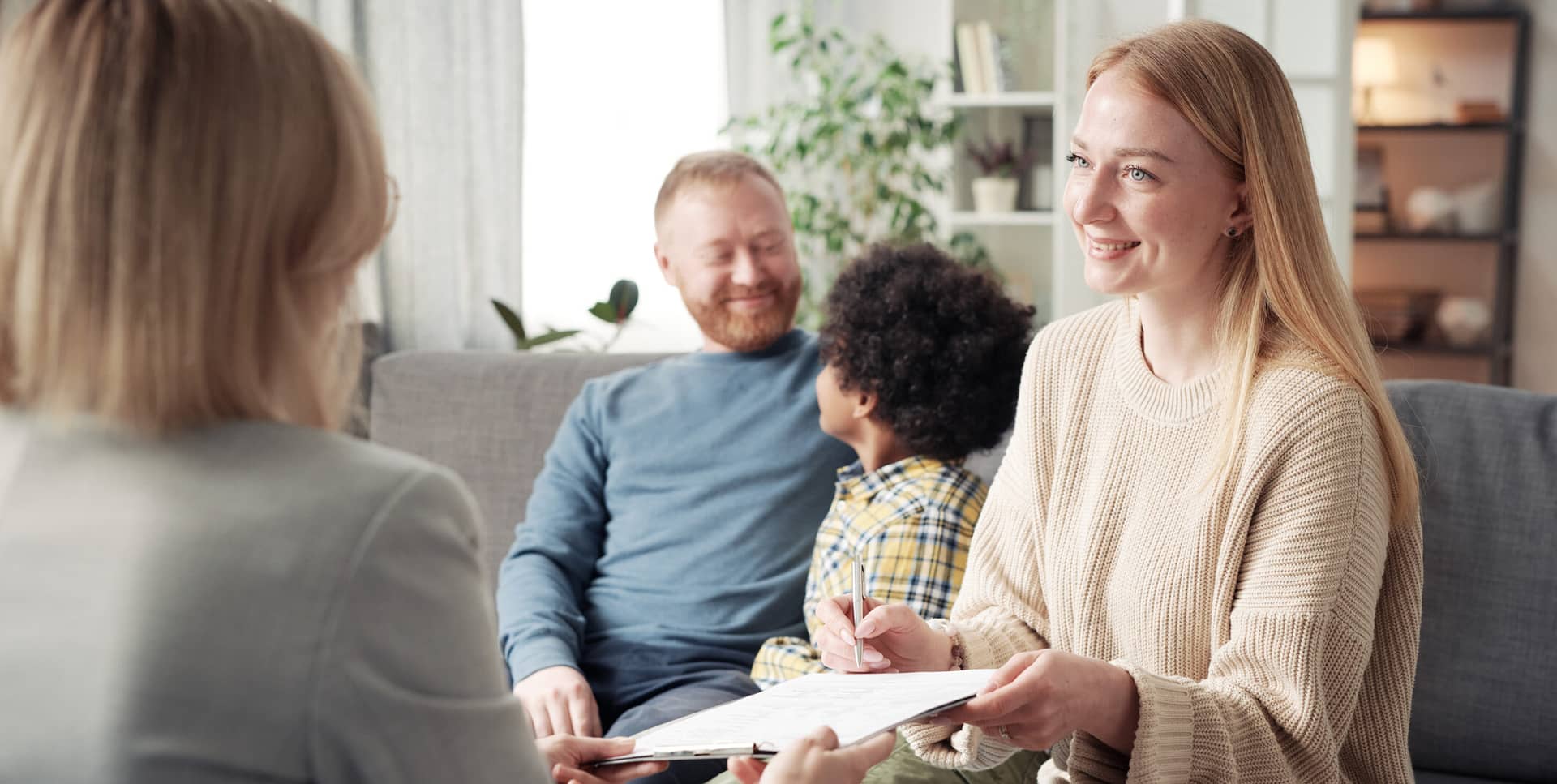 Happy young woman signing a document in her home with man and kid behind her