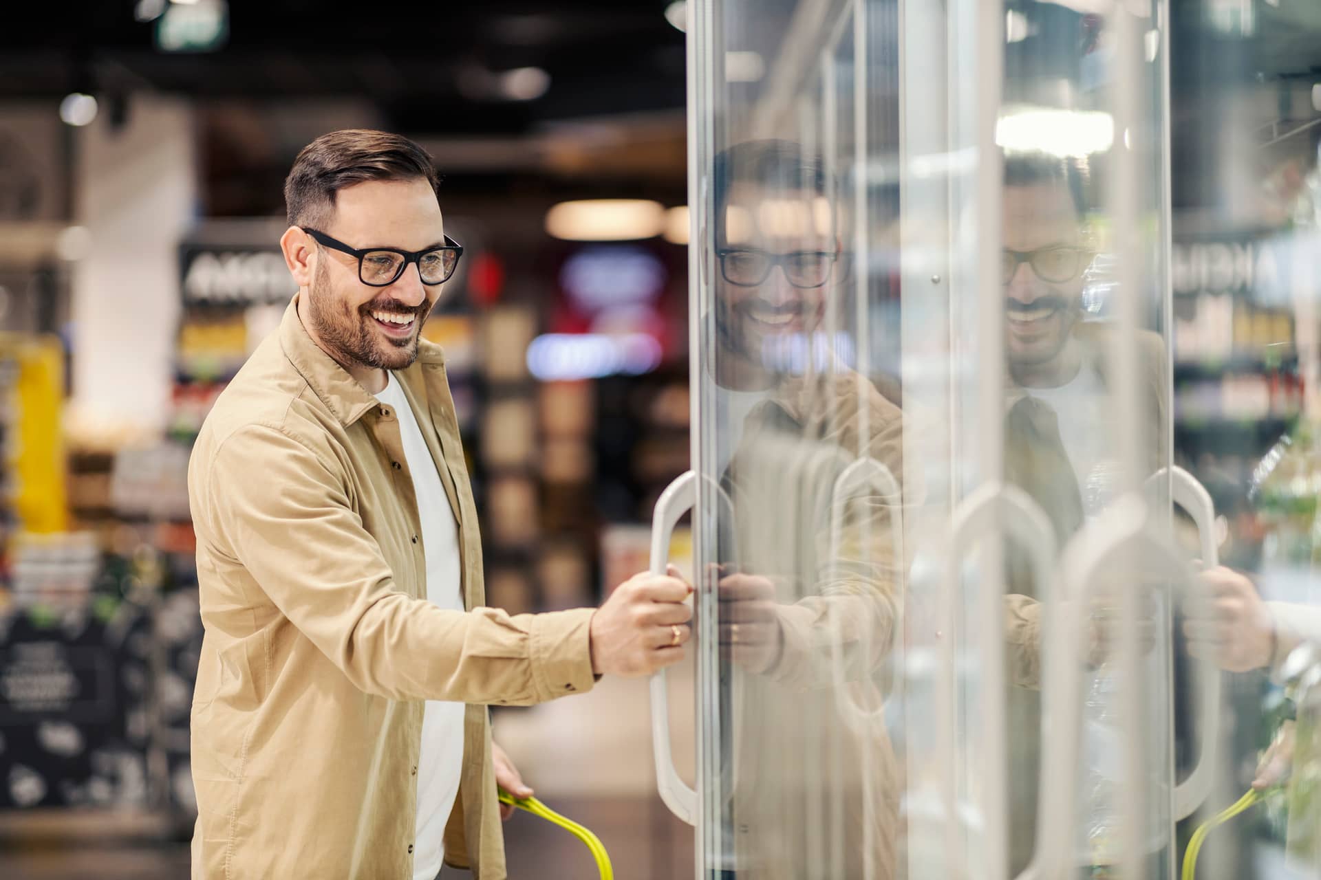 A happy man is choosing groceries from fridge at the supermarket.