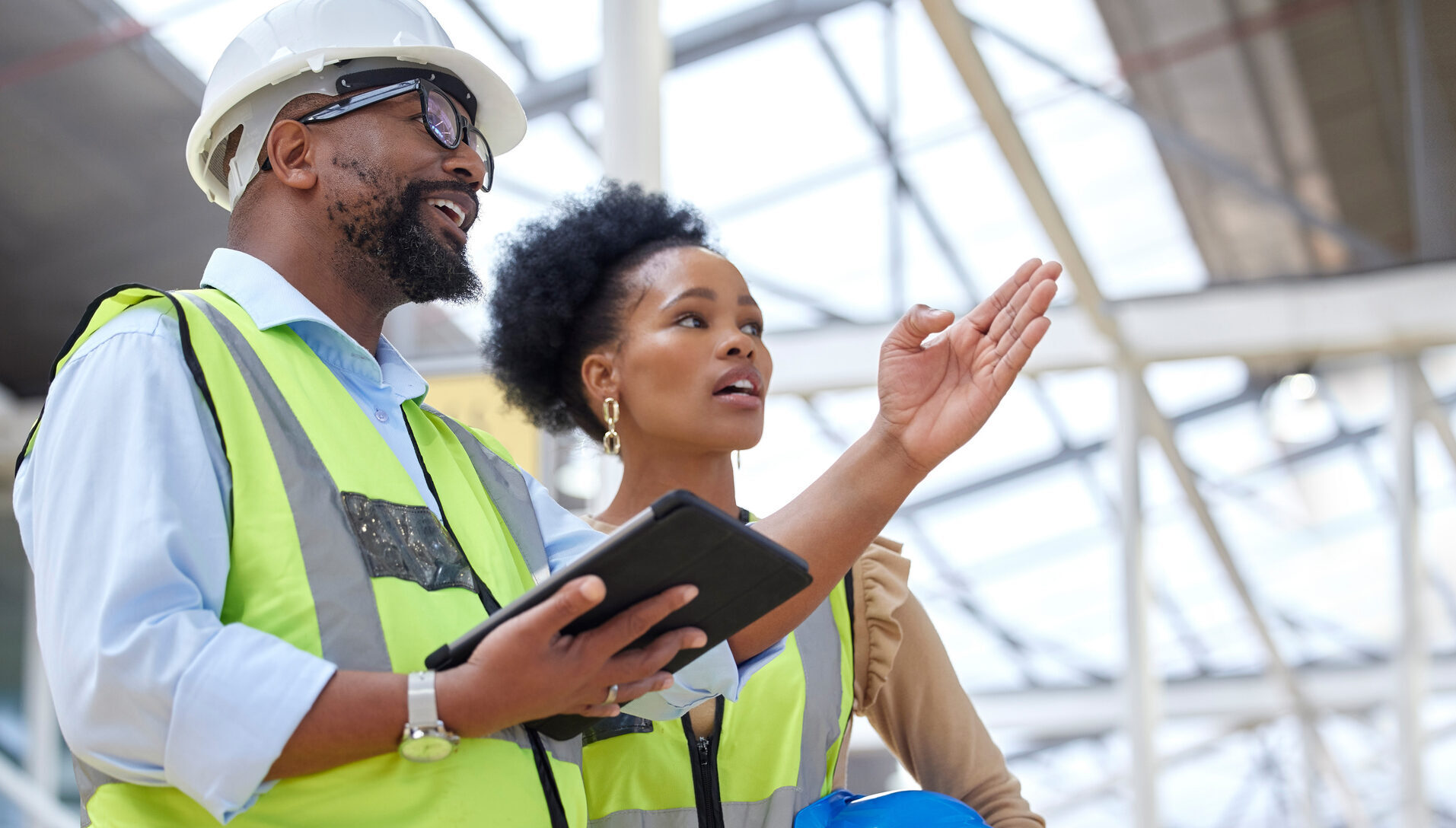 African American man and woman talking at a job site wearing hard hats and bright yellow vests