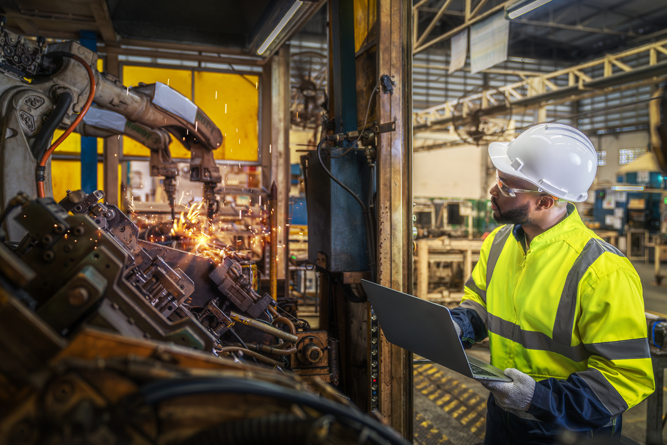 African American worker in a state-of-the-art factory with a robot auto welding machine assembling a metal part