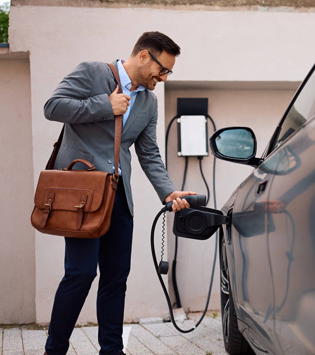 Happy man plugging in his electric car to charge.