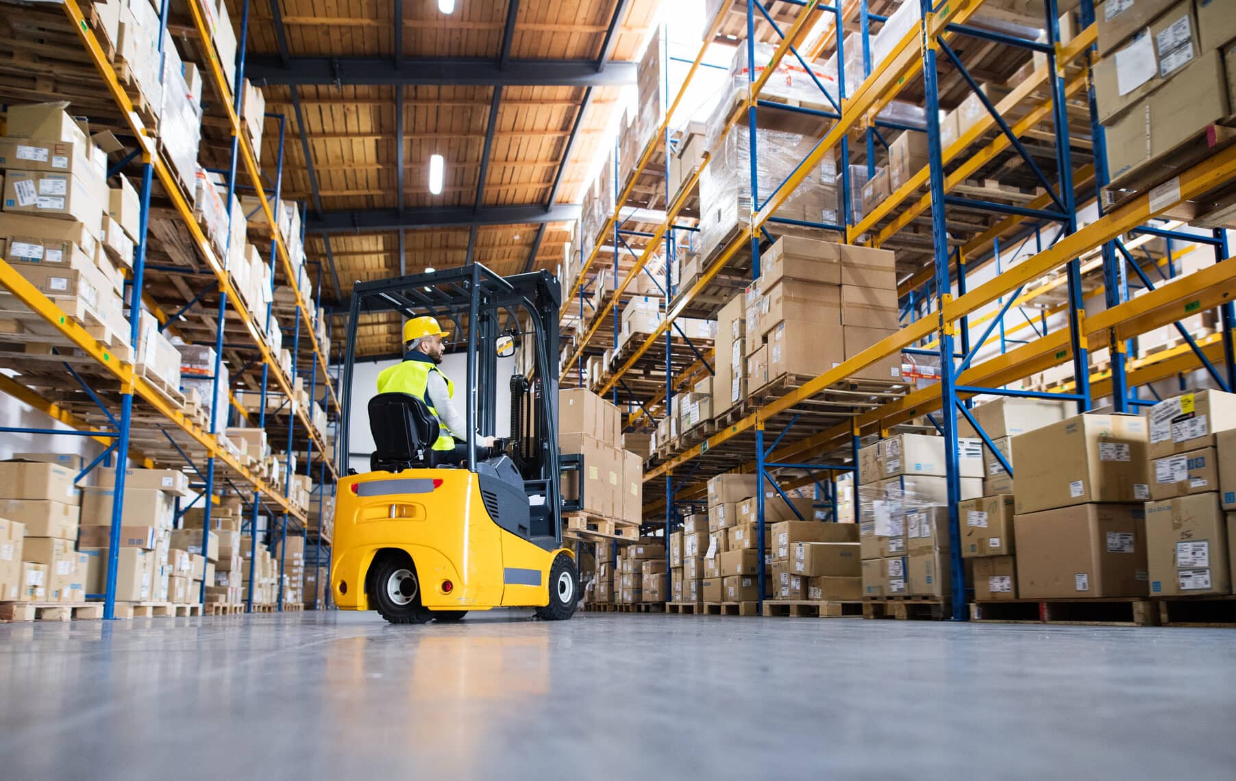 Young male worker lowering a pallet with boxes. Forklift driver working in a warehouse.
