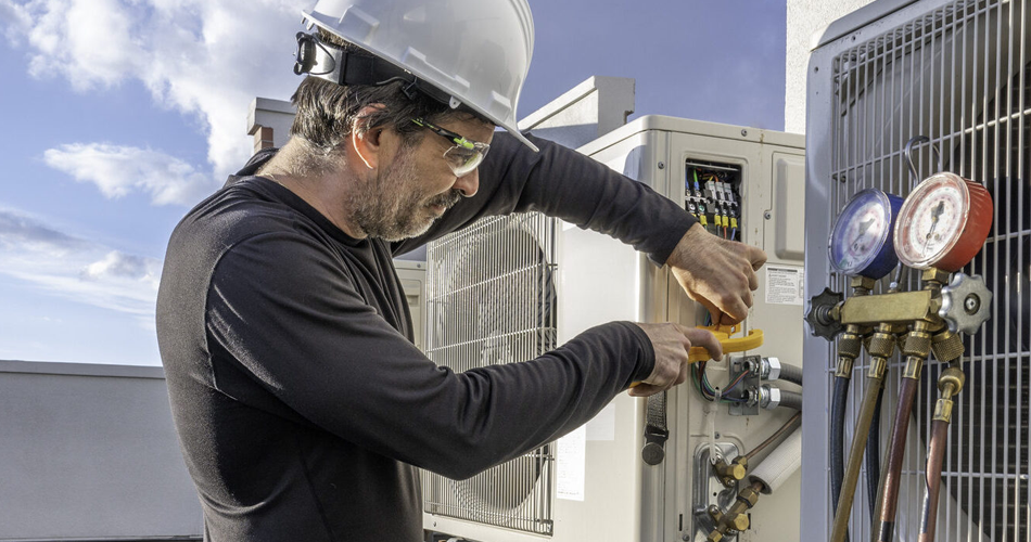 Close up of a man installing an AC unit on top of a building.