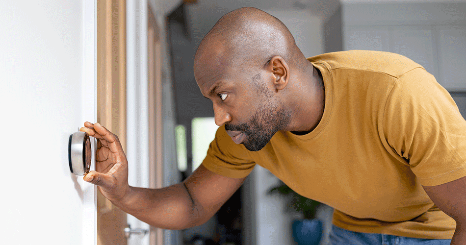 Young man adjusting smart thermostat temperature installed on a white wall.