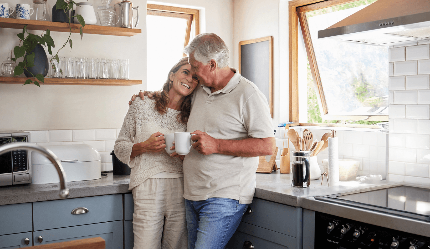 Elderly man and woman hugging while drinking a cup of coffee in their kitchen