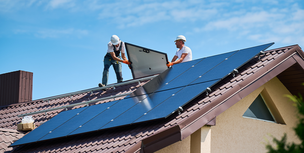 Two young men installing solar panels on top of a home