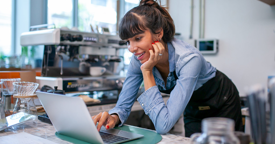 Woman using her laptop and smiling in a coffee shop kitchen