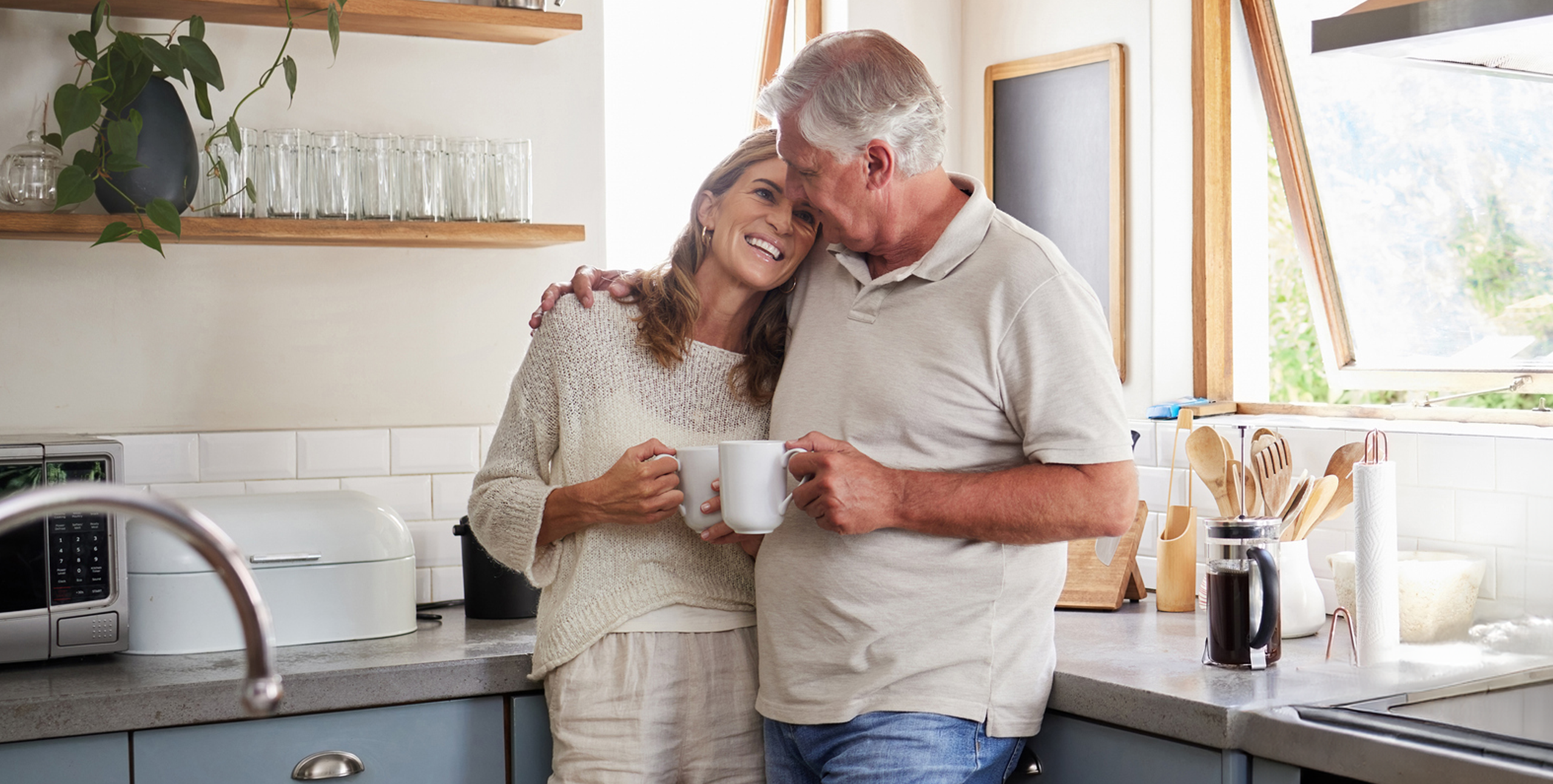 Elderly man and woman hugging while drinking a cup of coffee in their kitchen