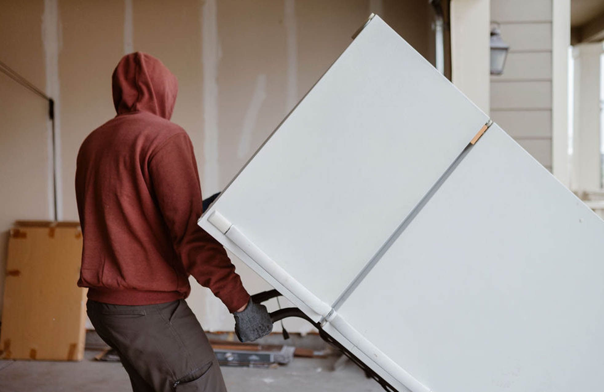 Man hauling away white refrigerator wearing a red hoodie.