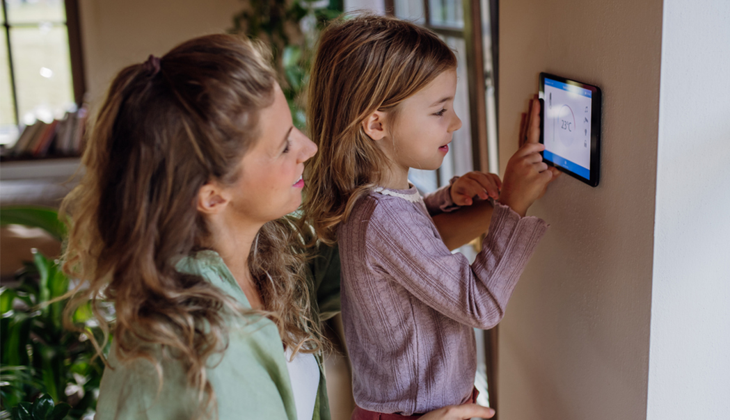 Mom and daughter decreasing temperature on wall thermostat to save energy