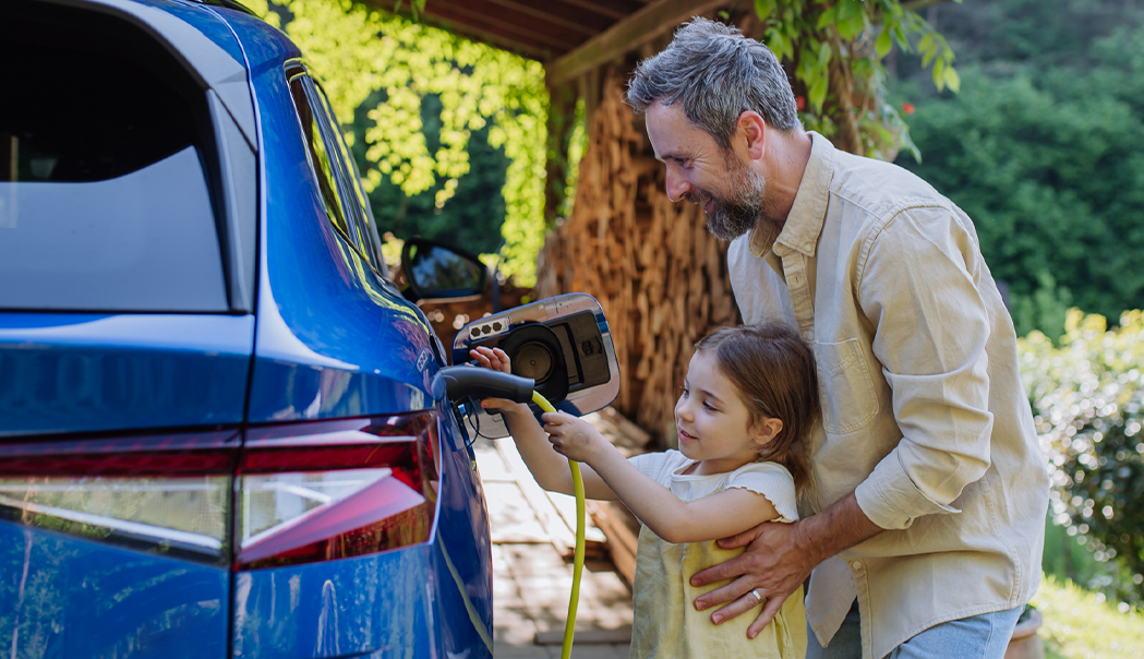 Older man helping young female kid plug EV charger into electric van