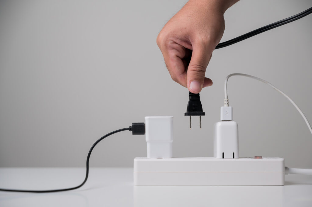 Hand holding electric plug, plugging into power strip